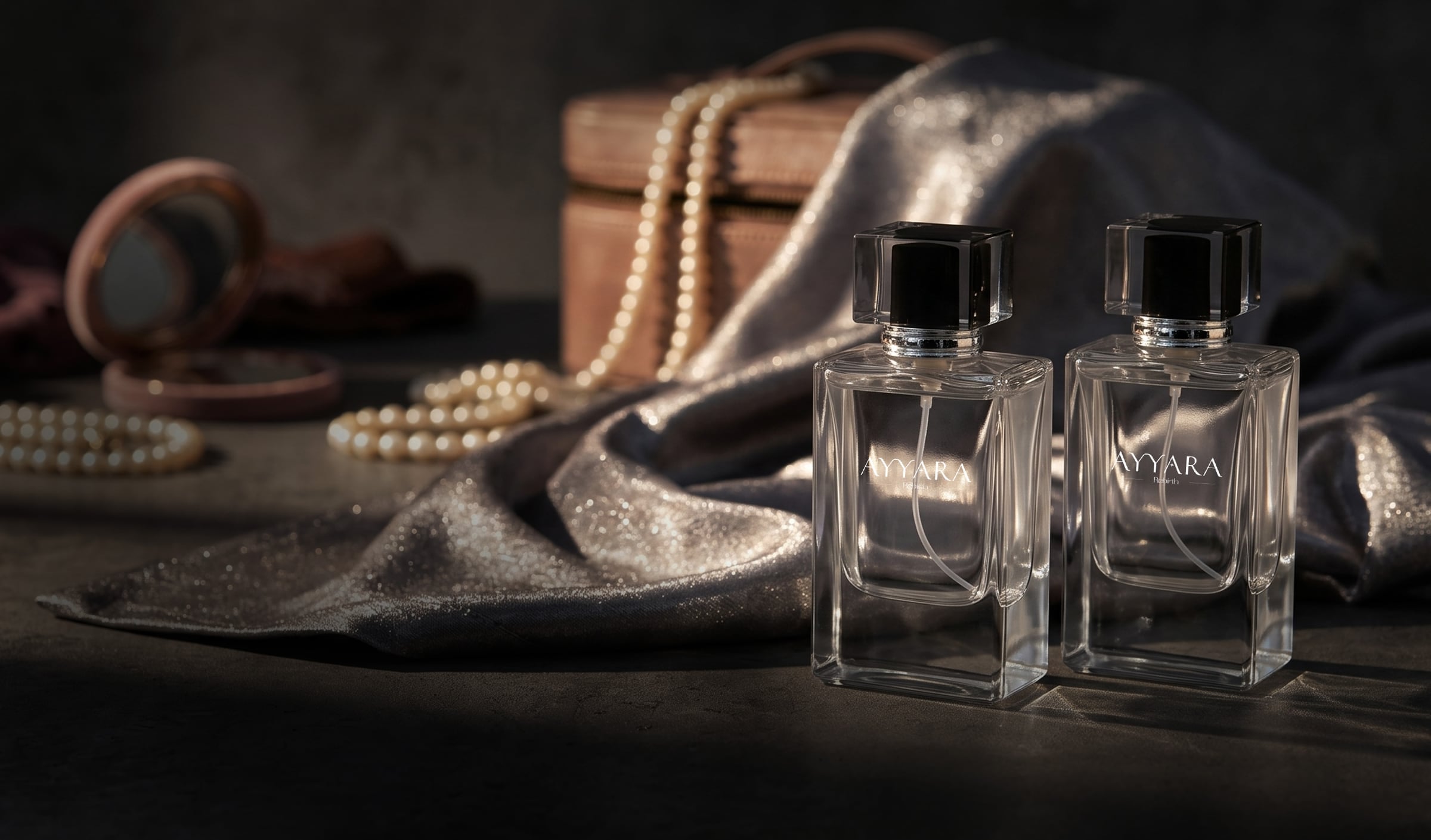Two Ayyara Rebirth bottles beside pearls and silver silk, with a jewellery box behind